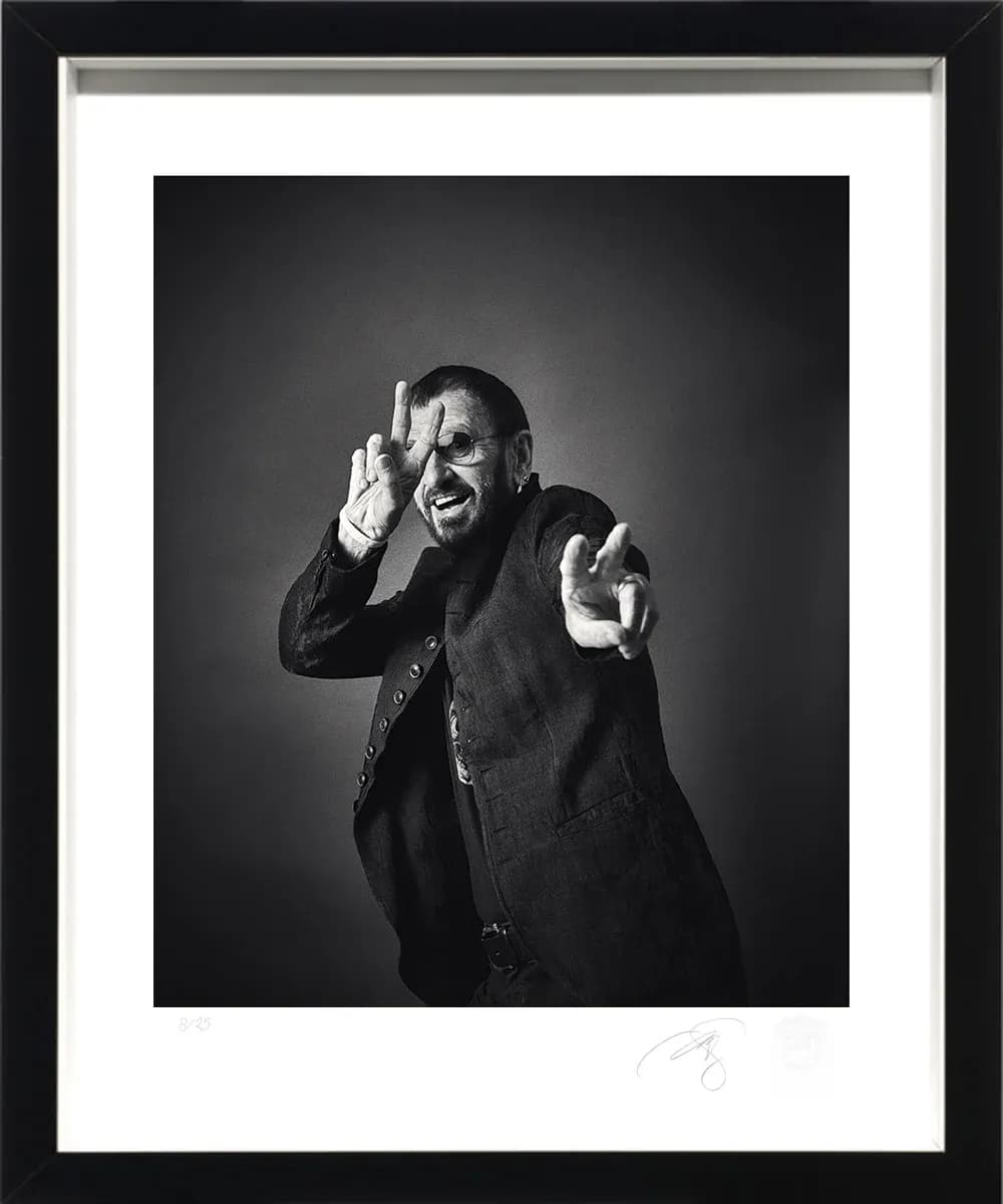 A framed and signed black and white portrait of Ringo Starr by photographer Andy Gotts, raising a peace sign beside his face, hung as an editioned exhibition print.