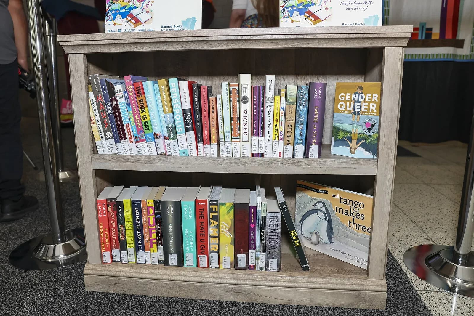 A wooden bookshelf at the 2026 American Library Association Annual Conference in Chicago displays frequently challenged books, with Maia Kobabe's Gender Queer facing out on the top shelf.